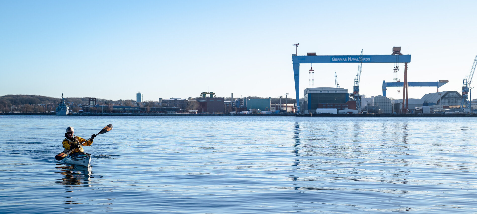 Kanufahrer auf der Kieler Förde mit den Portalkrähnen im Hintergrund